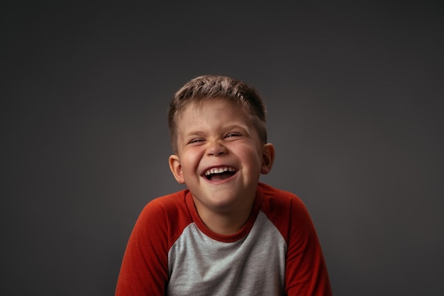 Lustiger lachender Junge im roten Hemd mit geschlossenen Augen glückliches Kind auf dunkelgrauem Hintergrund lustige Familienzeit ...