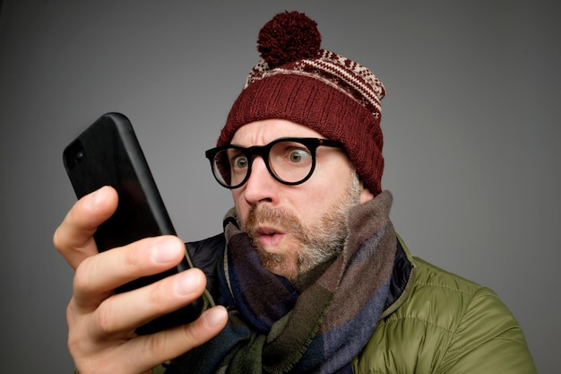 Lustiger Mann mit Brille und warmer Kleidung, der SMS auf grauem Hintergrund tippt