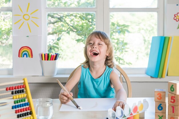 Lustiger schöner glücklicher Kinderjunge zeichnet lachend mit selektivem Fokus der Farbe