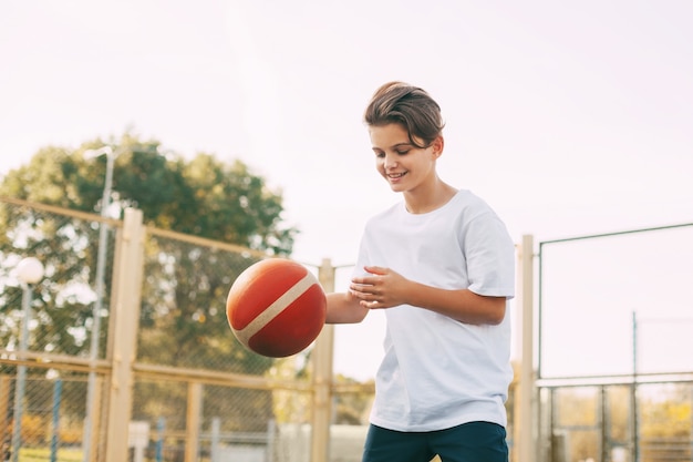 Foto lustiger süßer junge athlet führt den ball in einem basketballspiel. ein junge spielt nach der schule basketball