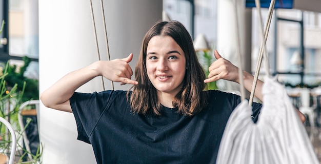 Lustiger Teenager sitzt in einer Hängematte in einem schwarzen T-Shirt