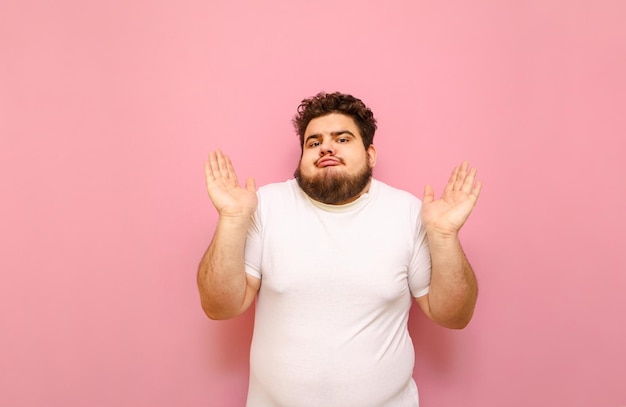 Lustiger verwirrter junger übergewichtiger Mann in weißem T-Shirt isoliert auf rosa Hintergrund blickt in die Kamera