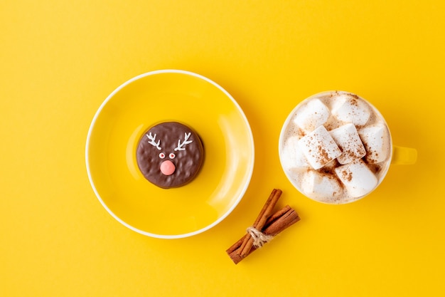 Lustiger Weihnachtsschokoladen-Rentier-Keks auf Tasse Untertasse und ein Kaffee mit Marshmallow auf Gelb