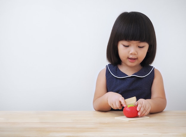 Lustiges asiatisches Kindermädchen, das mit hölzernem kochendem Spielzeug, kleiner Chef zubereitet Lebensmittel auf Küchenarbeitsplatte spielt.