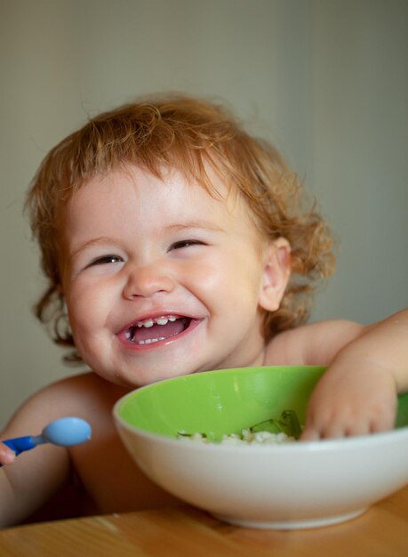 Lustiges Baby, das Essen selbst mit einem Löffel in der Küche isst Lächelndes Baby, das Essen isst