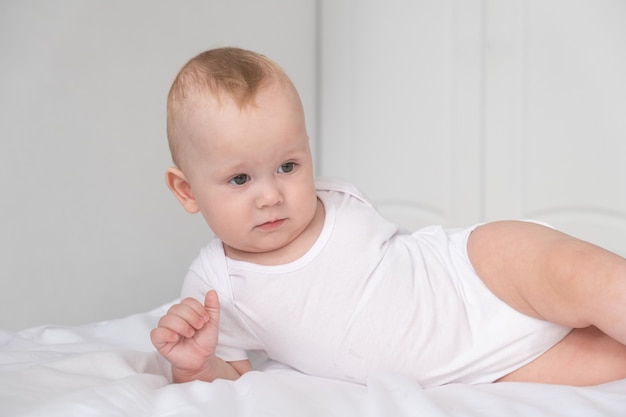 Lustiges Baby, das im weißen Schlafzimmer zu Hause lächelt.