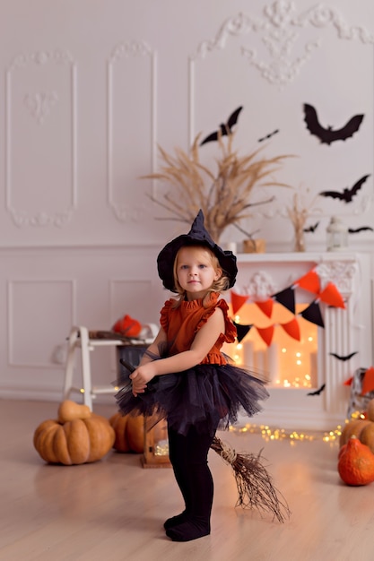 Foto lustiges baby im halloween-hexenkostüm mit kürbisheber und besen drinnen