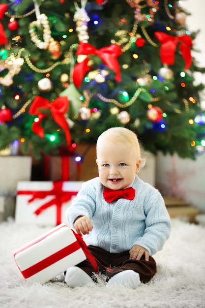 Lustiges Baby mit Geschenkbox und Weihnachtsbaum im Hintergrund