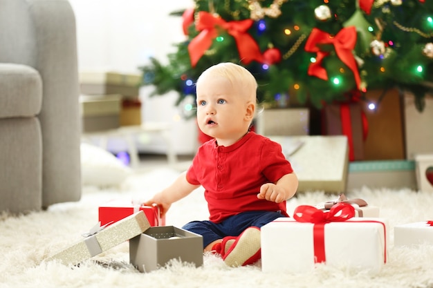 Lustiges Baby mit Geschenkboxen und Weihnachtsbaum im Hintergrund