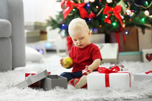 Lustiges Baby mit Geschenkboxen und Weihnachtsbaum im Hintergrund