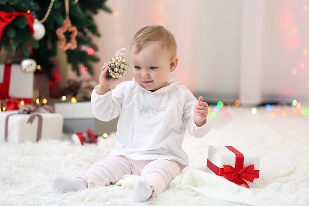 Lustiges Baby mit Geschenkboxen und Weihnachtsbaum im Hintergrund