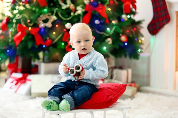 Lustiges Baby sitzt auf Schlitten und Weihnachtsbaum und Kamin auf der Oberfläche