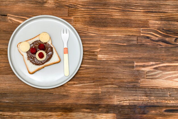 Lustiges Bärengesichtssandwichtoastbrot mit Erdnussbutter, Käse und Himbeere auf hölzernem Hintergrundkopienraum der Platte. Kinder Kind süßes Dessert Frühstück Mittagessen Essen.