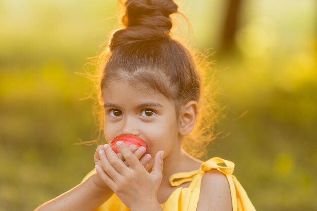 Lustiges dunkelhäutiges kleines Mädchen isst einen Apfel im Garten Gesunder Snack für Kinder