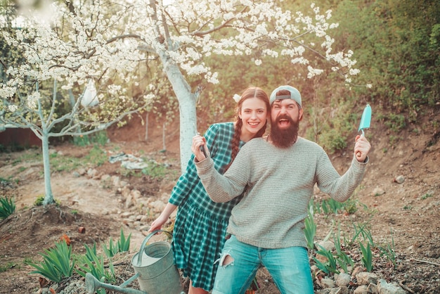 Lustiges Gärtnerpaar, das Gartenwerkzeuge am Frühlingsnaturhintergrund hält Paar Gärtner mit Gard