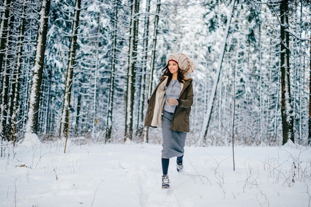 Lustiges junges attraktives Mädchen mit einem Turban vom Schal, der unter Bäumen im Schneewald läuft