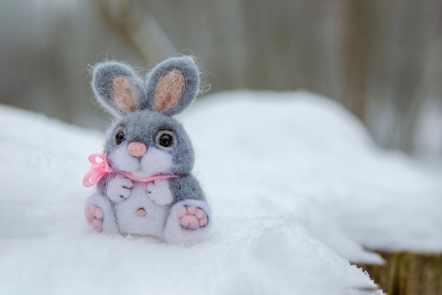 Lustiges Kaninchen im Schneeweihnachts- oder Osterkonzept ein grauer Spielzeughase sitzt in einer Schneewehe gegen den Hinter...