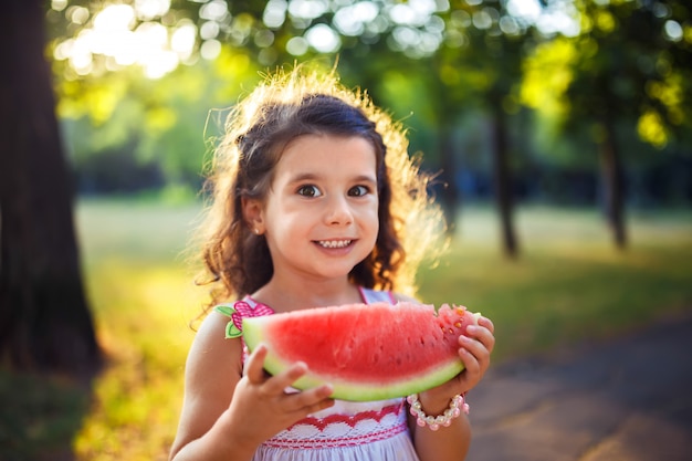 Lustiges Kind, das Wassermelone draußen im Sommerpark isst, Fokus auf Augen. Kind, Baby, gesundes Essen.