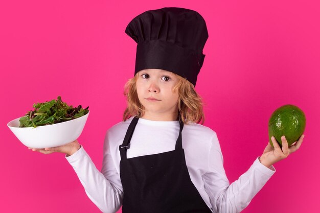 Lustiges Kind Koch mit Avocado und Gemüse Porträt des kleinen Kindes in Uniform des Kochs Chef Junge isoliert auf Studio-Hintergrund Nettes Kind, ein Koch zu sein Kind als Kochmütze verkleidet