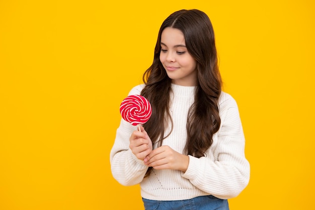 Lustiges Kind mit Lutscher über gelbem isoliertem Hintergrund Süßes Kindheitsleben Teenie-Mädchen mit leckerem Karamell-Lollipop-Süßigkeitenladen Glückliches Gesicht positive und lächelnde Emotionen von Teenager-Mädchen