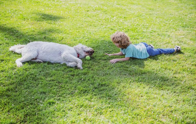 Lustiges Kind und Hund, die auf dem Gras liegen Fröhlicher Junge, der mit Hund im Garten spielt