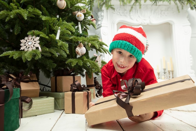 Lustiges Kind zu Weihnachten Junge unter dem Weihnachtsbaum mit Geschenken