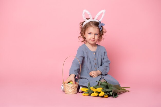 Lustiges Kindermädchen, das Hasenohren trägt und buntes Osterei hält.