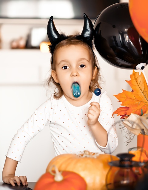 Lustiges Kindermädchen im bösen Kostüm für Halloween, das Bonbons Lolly Pop isst und Spaß hat.