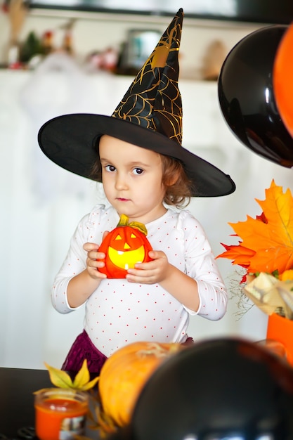 Lustiges Kindermädchen im Hexenkostüm für Halloween mit Kürbis Jack in den Händen