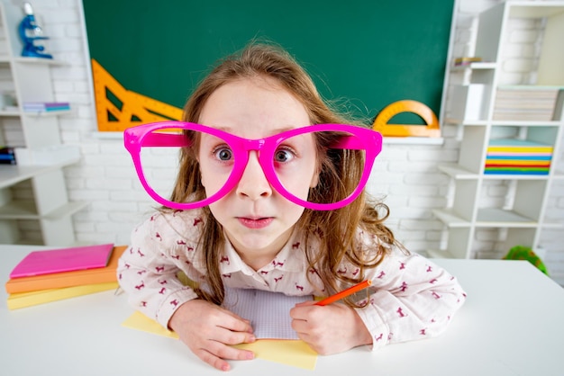 Lustiges Kinderschulmädchen mit lustiger Brille im Klassenzimmer