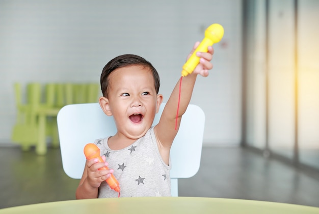 Lustiges kleines asiatisches Baby singen ein Lied durch Plastikmikrofon am Klassenzimmer.