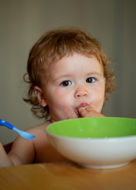 Lustiges kleines Baby in der Küche, das mit den Fingern vom Teller isst, gesunde Ernährung für Kinder