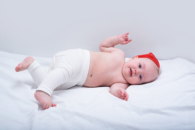 Lustiges kleines Baby in der Weihnachtsmütze, die auf Bauch ohne Kleidung liegt. weißer Hintergrund