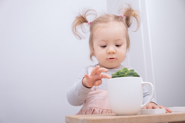 Lustiges kleines Mädchen berührt sorgfältig saftig im Topf.