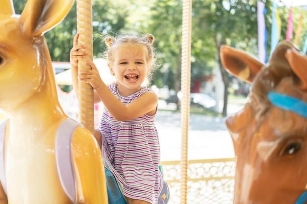 Lustiges kleines Mädchen in buntem Kleid fährt am Sommertag auf Karussell in einem Vergnügungspark