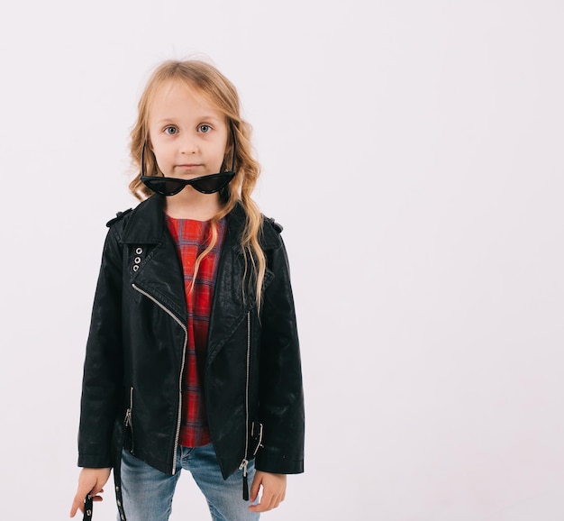 Lustiges kleines Mädchen in Lederjacke und Sonnenbrille hört Rockmusik auf weißem Hintergrund