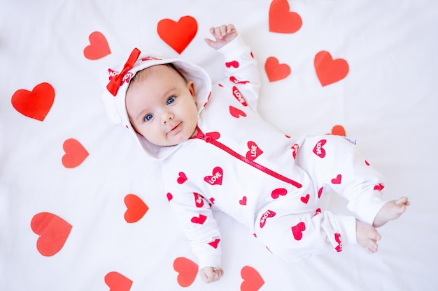 Lustiges kleines Mädchen mit roten Herzen auf einem Bett auf einem weißen Baumwollbett lächelnd oder lachend Valentinstag-Konzept