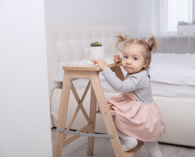 Lustiges Kleinkindmädchen, das mit Spielzeugen zu Hause im weißen Raum spielt.