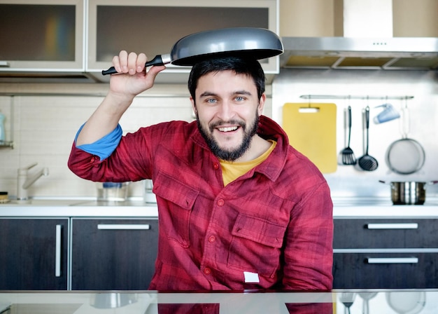 Lustiges Kochen Attraktiver kaukasischer Mann in der Küche mit tropfender Pfanne auf dem Kopf