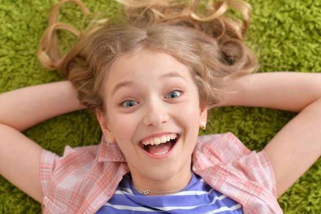 Lustiges lächelndes kleines Mädchen, das auf grünem Teppich liegt