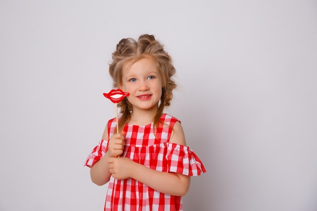 Lustiges lächelndes Sommerkleid des kleinen Mädchens auf weißem Hintergrund. Baby mit einem Lippenzubehör auf einem Stock.