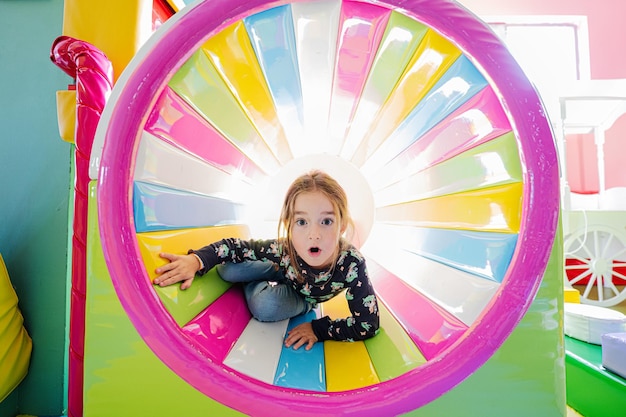 Lustiges Mädchen, das auf dem Spielplatz im Indoor-Spielzentrum in farbiger Röhre spielt