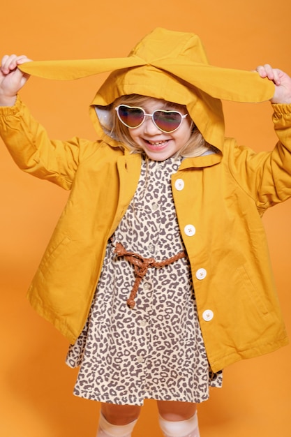 Lustiges Mädchen im gelben Regenmantel mit den Hasenohren auf gelbem Hintergrund