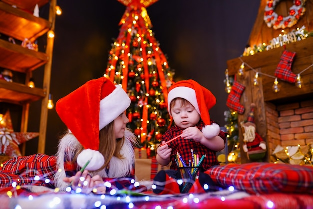 Lustiges Mädchen in Nikolausmütze schreibt Brief an Santa und ihren kleinen Bruder