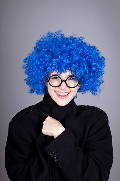 Lustiges Mädchen mit blauen Haaren in Brille und schwarzem Mantel.