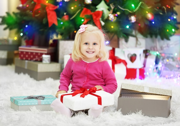 Lustiges Mädchen mit Geschenkboxen und Weihnachtsbaum im Hintergrund