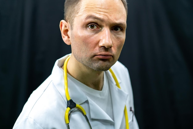 Lustiges Porträt eines jungen Arztes in einem weißen Kittel auf schwarzem Hintergrund Der Arzt schaut aufmerksam in die Kamera