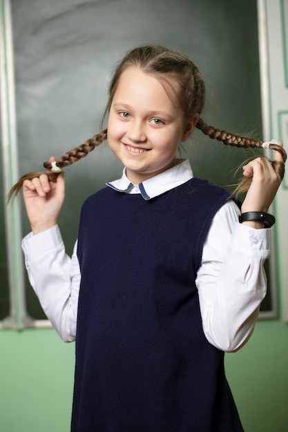 Lustiges Schulmädchen mit Zöpfen im mittleren Schulalter auf dem Hintergrund der Tafel