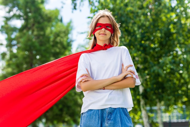 Foto lustiges teenager-mädchen, das power-superhelden über grünem parkhintergrund spielt