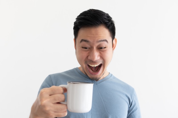 Lustiges Wowgesicht des Mannes im blauen T-Shirt trinkt Kaffee vom weißen Becher.